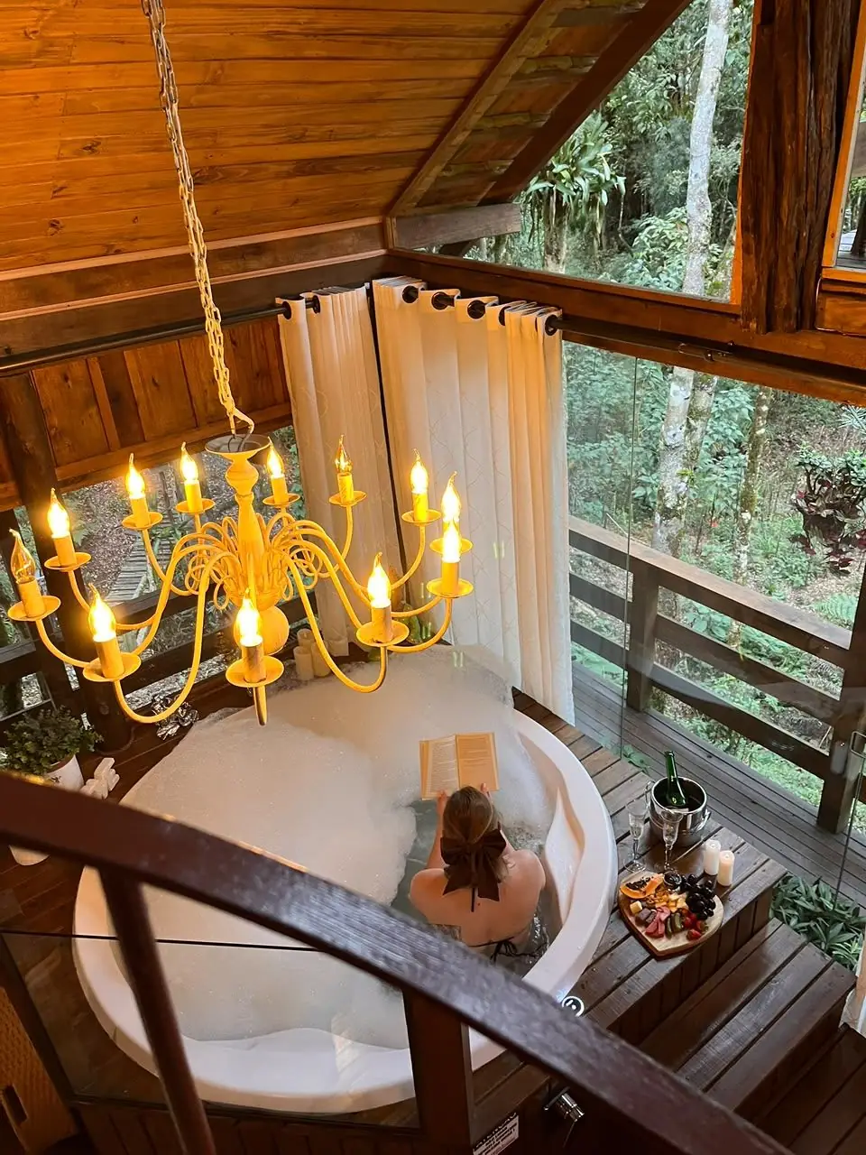 Hidromassagem redonda com lustre de velas, na varanda envidraçada da mata