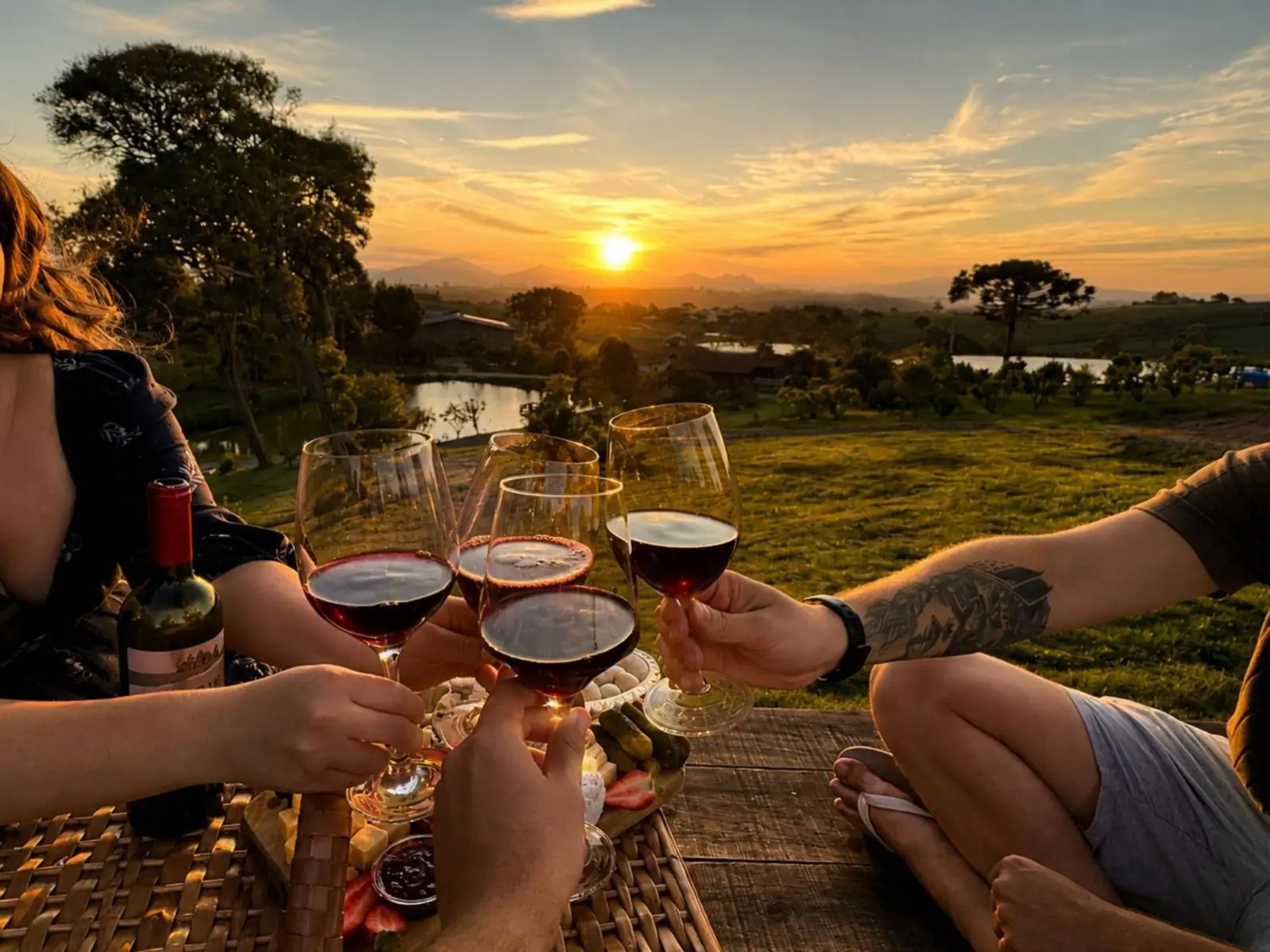 Brinde com vinho ao pôr do sol, com os lagos do sítio e a serra ao fundo